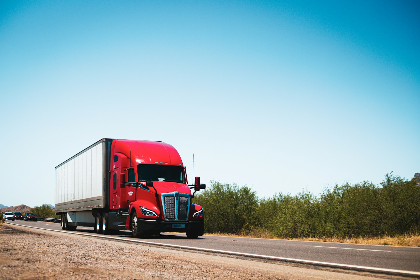 A red semi truck driving down a country road, commercial trucking